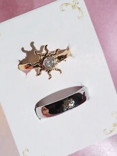 two different types of rings are in a white card with gold and silver designs on it