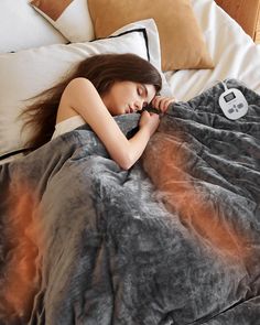 a woman laying in bed under a blanket with an electronic thermometer on it