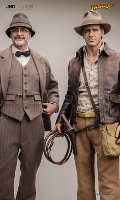 two figurines of men dressed in old west style clothing, one wearing a hat and the other holding a whip