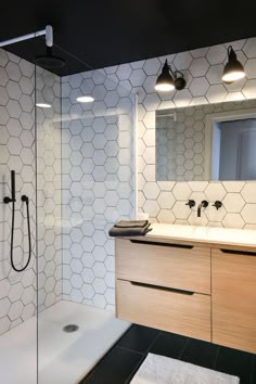 a modern bathroom with black and white tile on the walls, shower head, and vanity