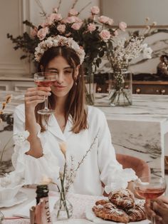 a woman sitting at a table holding a wine glass in front of her face with pastries on it