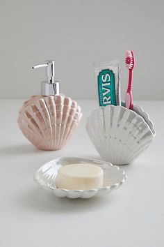 a soap dispenser and toothbrush holder on a white countertop next to a shell shaped soap dish