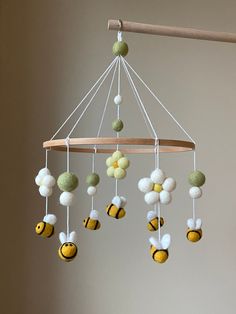 a mobile made out of felt balls hanging from a wooden rod with white and yellow flowers on it