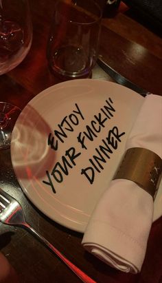 a white plate with writing on it sitting on a table next to silverware and wine glasses