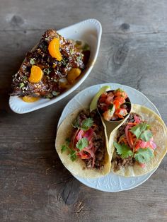 two tacos are sitting on a plate next to a bowl of salsa and another dish