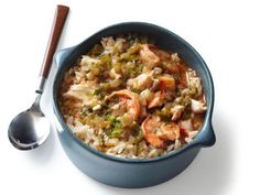 a blue bowl filled with rice and shrimp next to a spoon on a white surface