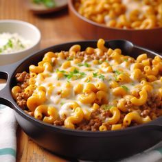 a skillet filled with macaroni and cheese on top of a wooden table