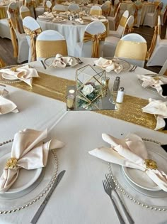 the table is set with white and gold linens, silverware, and napkins