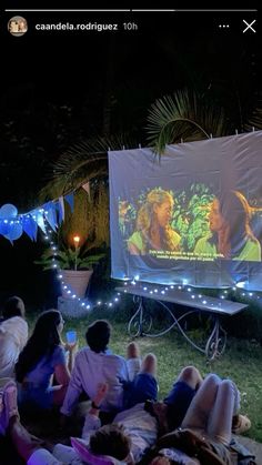 people sitting in the grass watching a movie on an outdoor projector screen at night