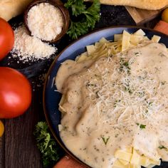 a blue plate topped with pasta covered in gravy next to tomatoes and parmesan cheese