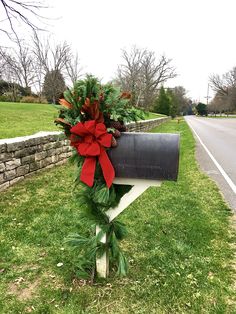 a mailbox decorated with red bows and greenery on the side of a road