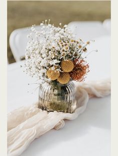 a vase filled with flowers sitting on top of a white table cloth covered tablecloth