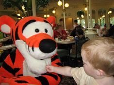 a small child is playing with a stuffed animal at a table in front of people