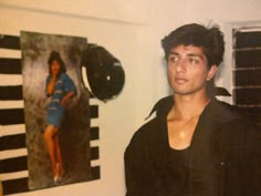 a young man standing in front of a wall with pictures on the wall behind him