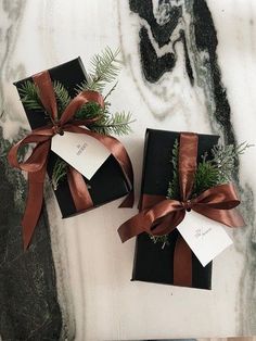 two black boxes with brown ribbons tied around them on a marble countertop next to a bottle of wine