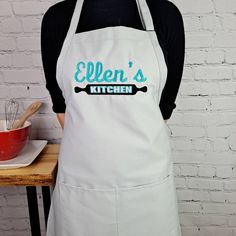 a woman wearing an apron with the words ellen's kitchen on it and a bowl of whisk next to her