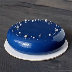 a blue cake sitting on top of a white plate covered in silver balls and water