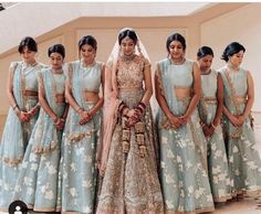 a group of women standing next to each other in front of a wall wearing blue dresses