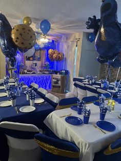 a room filled with tables covered in blue and white tablecloths, balloons and decorations