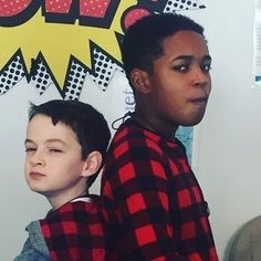 two young boys standing next to each other in front of a wall with comic signs on it