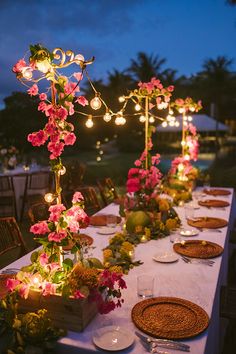 an outdoor dinner table with flowers and lights on the top is set up for a party