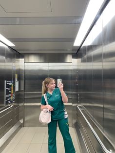 a woman in scrubs taking a selfie with her cell phone while standing in an elevator