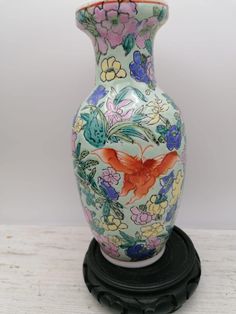 a colorful vase sitting on top of a black stand with flowers and butterflies painted on it