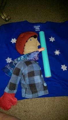 a doll laying on the ground next to a blue t - shirt with snowflakes