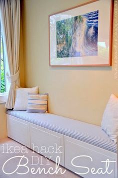 a white bench sitting in front of a window next to a painting on the wall