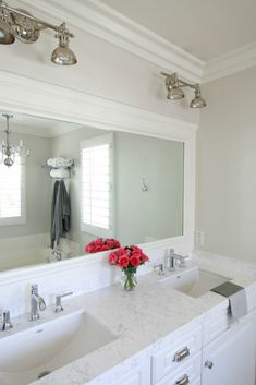 a bathroom with two sinks and a large mirror over it's sink area that has red flowers on the counter