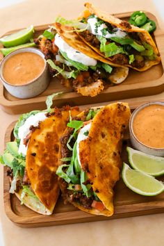 three tacos with sauces and lettuce are on a wooden platter