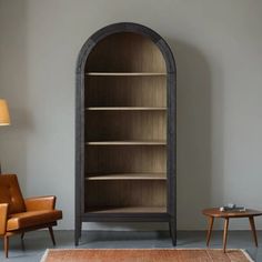 a living room with a chair, table and bookshelf in front of a gray wall