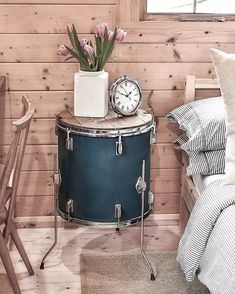 a green drum sits next to a small table with a clock on it and flowers in a vase