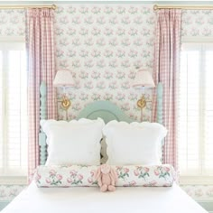 a bedroom with pink and green floral wallpaper, white bedding and two lamps on either side of the headboard