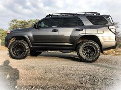 a gray four - doored suv parked on the side of a dirt road with trees in the background