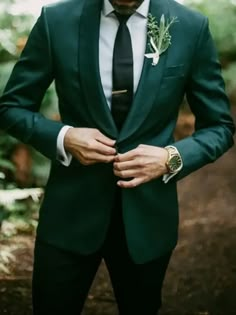 a man in a green suit and tie is looking down at his hand on his lapel