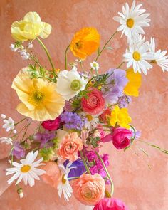 a vase filled with lots of colorful flowers on top of a pink table next to a wall