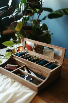 an open wooden jewelry box sitting on top of a table next to a potted plant