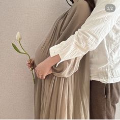 a pregnant woman holding a flower while standing next to a man