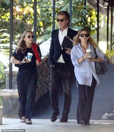 three people walking down the street with coffee in their hands and one person holding a cell phone