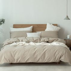 an unmade bed with beige linens and pillows on the headboard in a white room