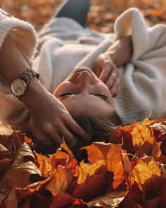 a woman laying on top of leaves in the fall