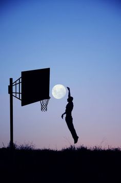 a person jumping up into the air to dunk a basketball in front of a full moon