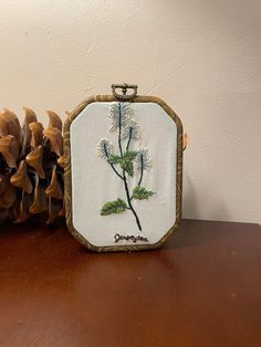 a pine cone sitting on top of a wooden table next to a small embroidered frame