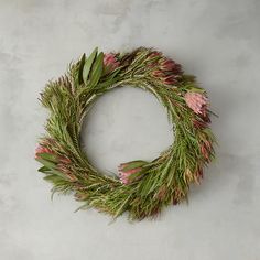 a wreath with pink flowers and greenery hanging from the side on a gray wall