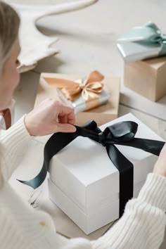 a woman opening a white gift box with a black ribbon