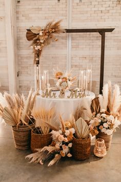 a table topped with lots of flowers next to tall candles and wicker baskets filled with feathers