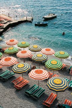 many beach chairs and umbrellas are on the sand near the water's edge