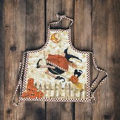 an apron is hanging on a wooden wall with pumpkins, witches and jack - o'- lanterns