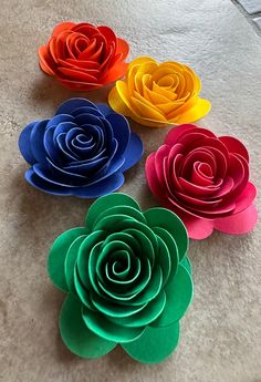 four different colored paper flowers sitting on the ground